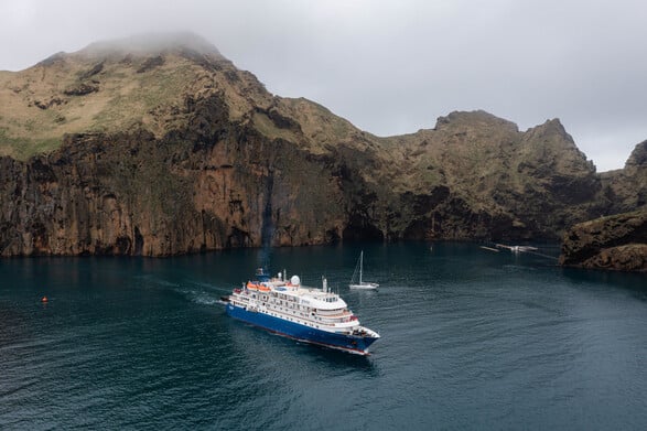 Das Kreuzfahrtschiff von Poseidon Expeditions und ein kleines Segelboot liegen in Island vor einem schroffen Bergpanorama